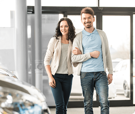 Young couple walking into a car dealership with the front of a shinny new car in the foreground