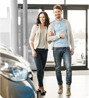 Young couple walking into a car dealership with the front of a shinny new car in the foreground