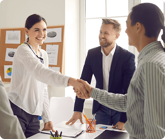 Three professionals in a room where a woman is shaking hands with a man across a desk